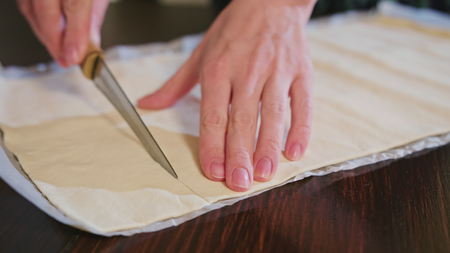 Woman cuts dough for baking knife, dough lying on white paperの写真素材