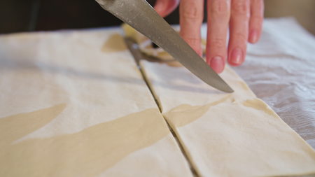 Woman cuts dough for baking knife, dough lying on white paper