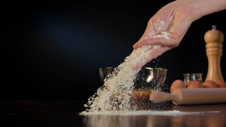 Female hand spilling flour on the table against a dark blue background. Close-up shot