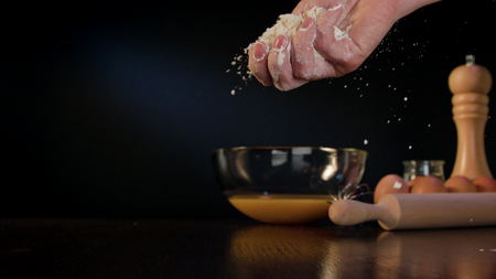 Female hand spilling flour on the table against a dark blue background. Close-up shotの写真素材