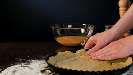 Female hands coating and spreading dough in a baking pan against a dark background. Close-up shot