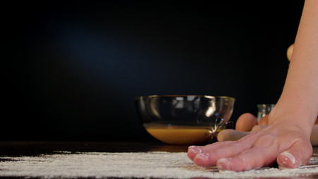Female hand spreading flour on the table against a dark blue background. Close-up shotの写真素材