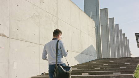A young man walking and using a smartphone outside. Medium Dolly shot