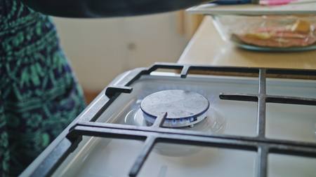 Woman roasting peanuts in a pan in the kitchen, lights a gas stove
