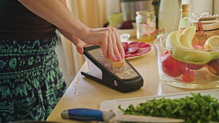 Woman rubs Parmesan cheese salad in the kitchen, preparing food