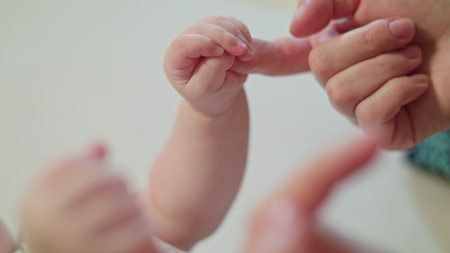 Baby is holding moms finger in a fistの写真素材