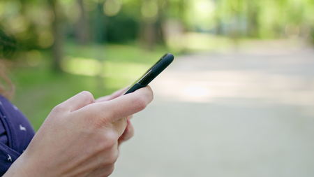 Woman taking a walk in the park using a cellphone. Dolly shot. Soft focus.