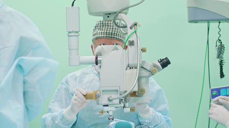 Team of ophtalmology surgeons and assistants with ophtalomological surgery tools during surgical treatment. Female and male surgeons operate the machinery. Indoor. Close up.の写真素材