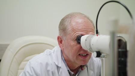 Male mid-aged ophtalmologist examines and talkes to the pacient. Indoor. Medium.