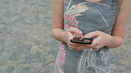 A young lady using a smapthone outdoors against a street paved with cobblestones background. Soft focus close-up shootの写真素材