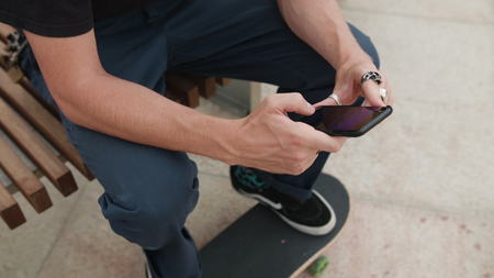 Young readhead hispter with beard and moustaches in jeans and T-shirt writes a message on smartfone. Outdoor. Cloudy. Medium. Stabilised. Portrait. From aboveの写真素材
