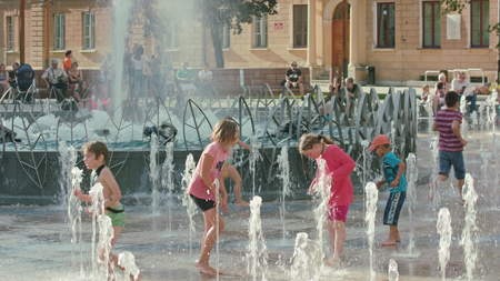 Lublin, Poland - July 2017: Kids are playing in fountain at hot sunny day during Festival Sztukmistrzow. Water gushes and splashes. People are sitting on the benches in the shadow on background. Metal elements of fountain are visible. Medium. Outdoor. Sunのeditorial素材