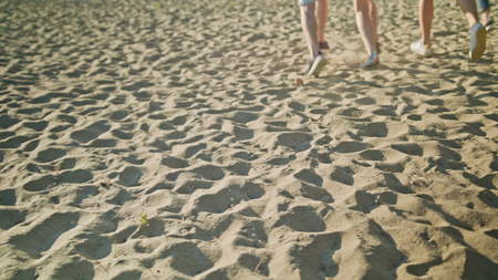 Feet running on the sand. Young people having fun on the beach. Medium shot. Dolly shot. Soft Focus.