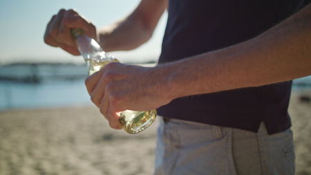 A young man on the beach opening a bottle. Closeup shoot. Soft focus.の写真素材