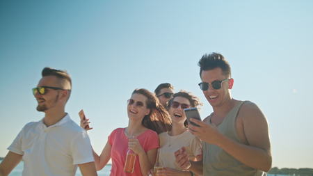 Young people having fun on the beach using phones. Medium shot. Soft Focus.