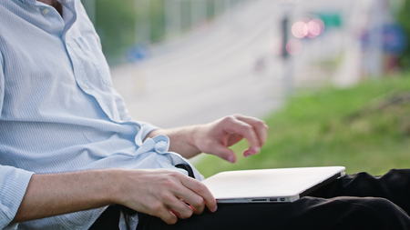 A young man using a laptop and sitting under the tree. Closeup shot. Soft focus.