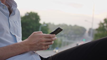 A young mans hands using a mobile outdoors. Closeup shot. Soft focus.
