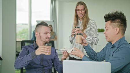 two people are working on a laptop in modern start up office a man brings coffeeの写真素材