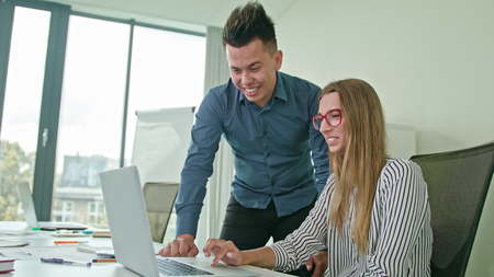 Two people in modern start up office male team leader pointing at screen discussing diverse people...