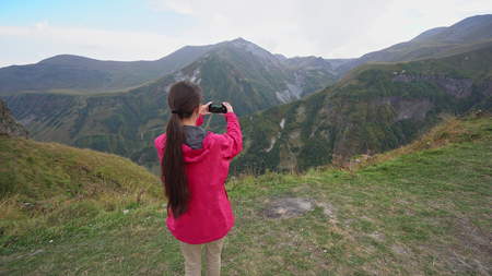 A young lady taking photos in the mountains. Long shot.