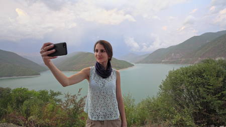 A young lady taking selfie near the lake in the mountains. Medium shot.