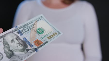 A woman in a white sweater receiving cash (US Dollars) against a black background. Close-up shotの写真素材