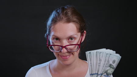 A woman in a white sweater holding cash (US Dollar banknotes) against a black background. Close-up shotの写真素材