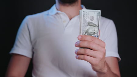 A man wearing a white t-shirt holding cash (US Dollars) against a black background. Close-up shotの写真素材