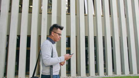 A young man walking and using a smartphone outside. Medium Dolly shot