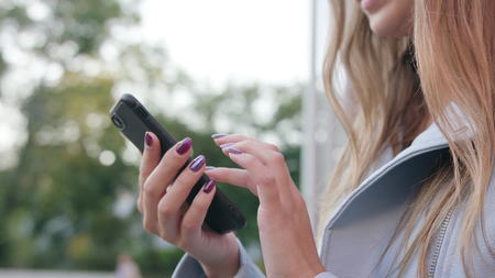A young lady using a smartphone outdoors. Close-up shot. Soft focus.の写真素材