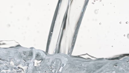 Macro footage of water pouring in a transparent container. White background. Close-up macro shot.