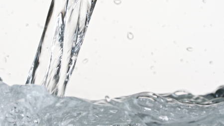 Macro footage of water pouring in a transparent container. White background. Close-up macro shot.の写真素材