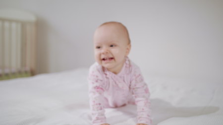 A baby crawling on all fours on a white bed at home. Close-up shot. Soft focusの写真素材