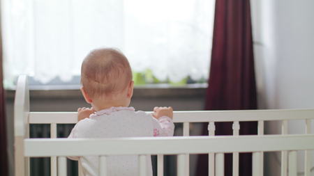 Babys standing in a white crib at home and playing. Medium shot.の写真素材