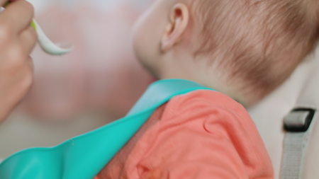 A baby girl eating puree at home. The baby doent want to eat. Close-up shot. Soft focus.の写真素材