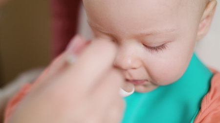 A baby girl eating puree at home. Close-up shot. Soft focus.の写真素材