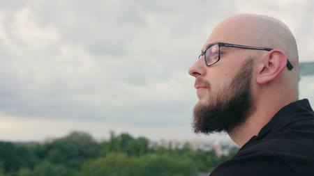 A man with a beard wearing black glasses looks into the distance. Close-up shot. Soft focus