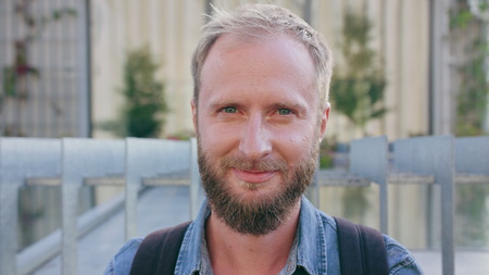 A happy smiling red-haired man with a beard wearing a backpack in the city street. Close-up shot....