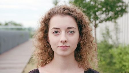 A young woman with a curly hair putting on headphones in the city street. Close-up shot. Soft focus
