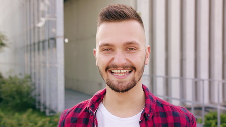 A young man with a beard smiling in the city street. Close-up shot. Soft focusの写真素材