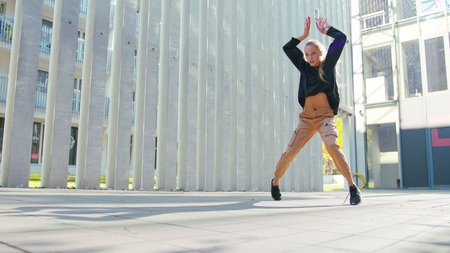 A young girl performs modern hip hop dance on the streets of the city during the summer, twisting and rotating.の写真素材