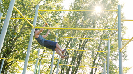 Handsome muscular man doing exercises on horizontal bar outdoors. Calisthenics workout. Slim athlete...