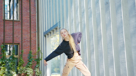 A young girl performs modern hip hop dance on the streets of the city during the summer, twisting...