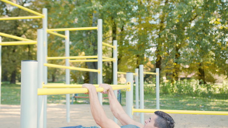 Handsome muscular man doing exercises on horizontal bar outdoors. Calisthenics workout. Slim athlete...