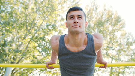 Handsome muscular man doing exercises on horizontal bar outdoors. Calisthenics workout. Slim athlete...
