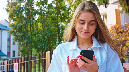 Woman texting on smartphone looking happy outside, Caucasian girl in her 20s happily texting on phone in public place, 4kの写真素材