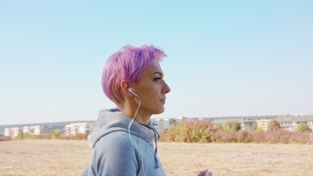 A young y with pink hair jogging in the suburbs. Close-up shot