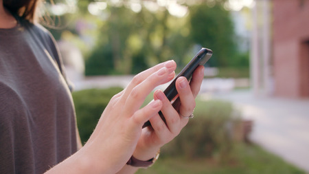 A close-up of a womans hand holding and using a phone outdoors. Soft focusの写真素材