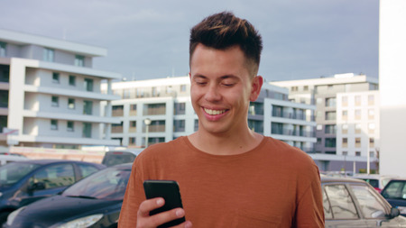 An attractive young man wearing an orange T-shirt walking and using a phone in town. Close-up dolly...