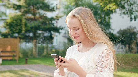 An attractive young blonde lady walking and using a phone in town. Close-up shot. Soft focus. Dolly shotの写真素材